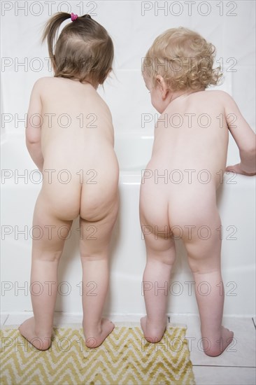 Naked Caucasian boy and girl standing near bathtub