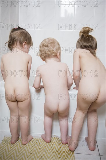 Naked Caucasian boy and girls standing near bathtub