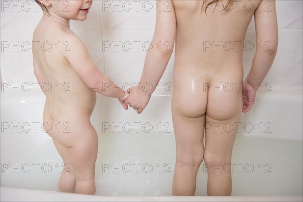 Naked Caucasian girls standing in bathtub holding hands
