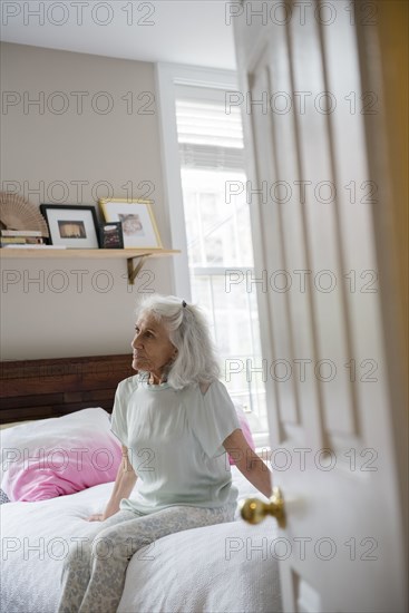 Older woman sitting on bed beyond doorway
