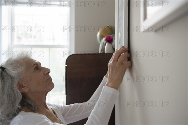 Older woman hanging artwork on wall