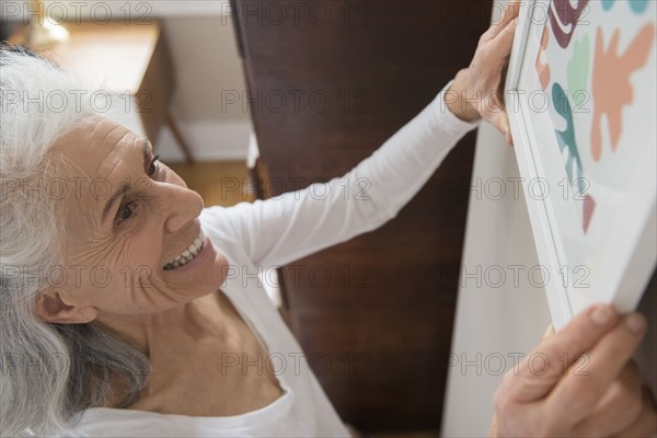 Older woman hanging artwork on wall