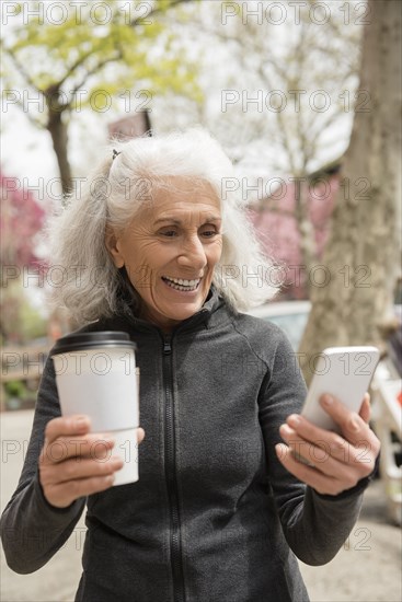 Older woman drinking coffee and texting on cell phone