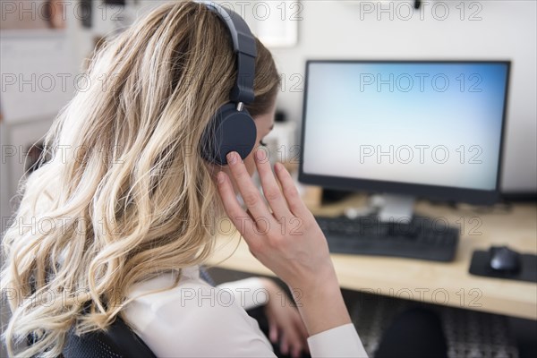 Caucasian woman listening to headphones at computer desk