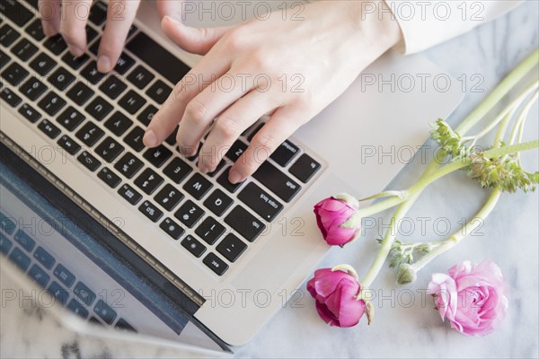 Hands of Caucasian woman typing on laptop near flowers