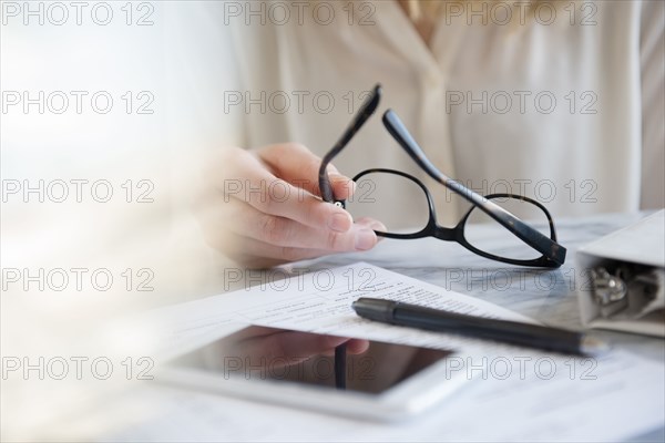 Hands of Caucasian woman holding eyeglasses near pen and cell phone