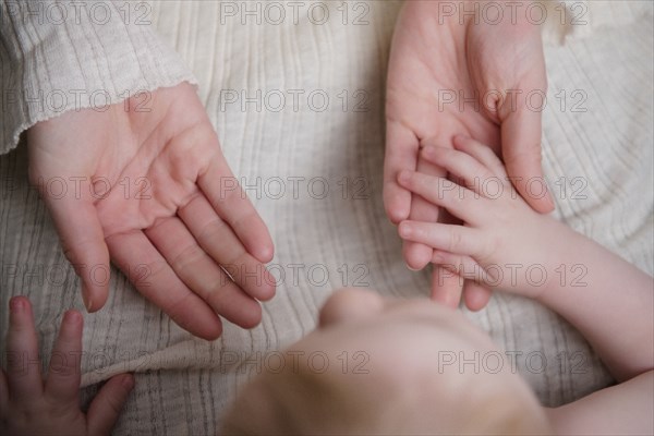 Caucasian baby boy holding hand of mother