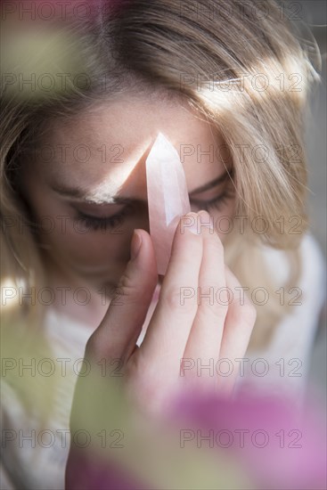 Caucasian woman holding crystal to forehead