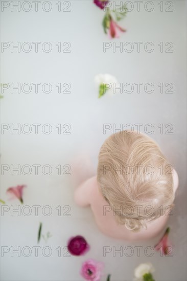 Caucasian baby boy in milk bath with flowers
