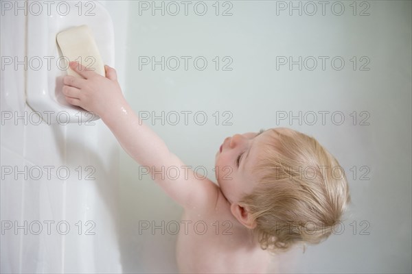Caucasian baby boy in milk bath reaching for soap