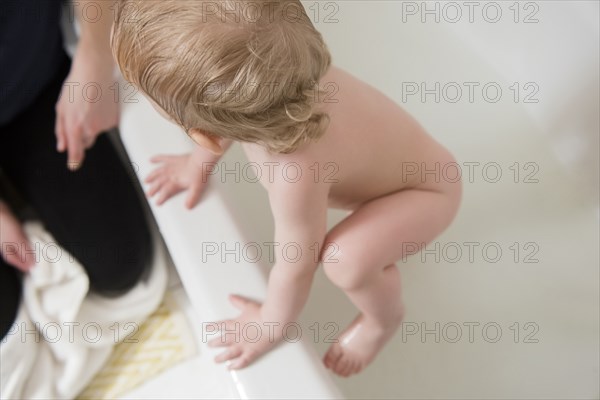 Caucasian baby boy climbing to mother from bathtub