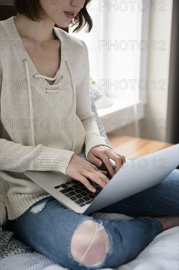 Caucasian woman sitting on bed using a laptop