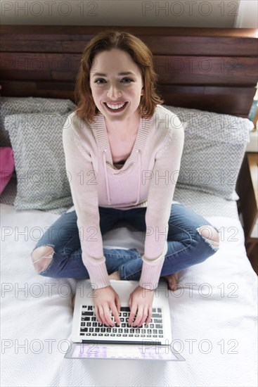 Caucasian woman sitting on bed using a laptop