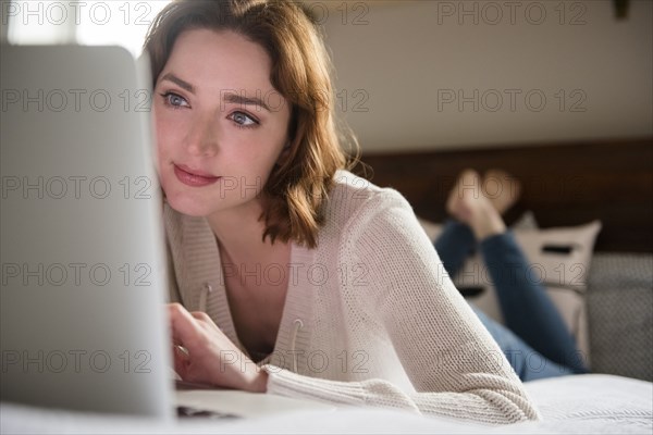Caucasian woman laying on bed using a laptop