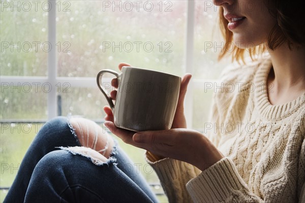 Caucasian woman drinking coffee near rainy window