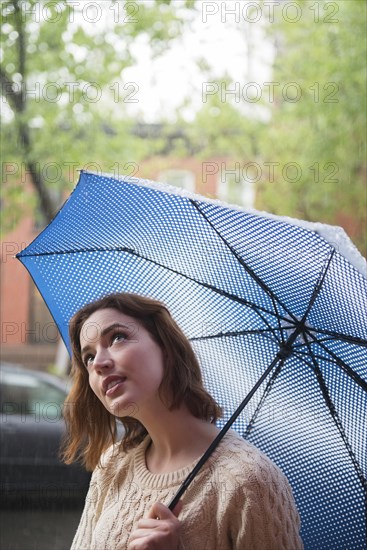 Caucasian woman holding umbrella looking up