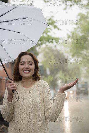 Carefree Caucasian woman holding umbrella in rain