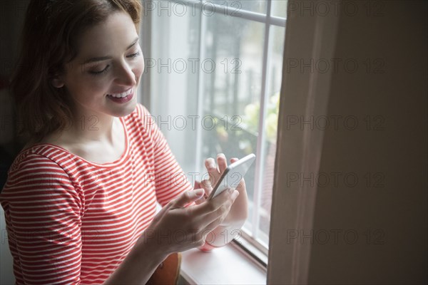 Caucasian woman texting on cell phone near window