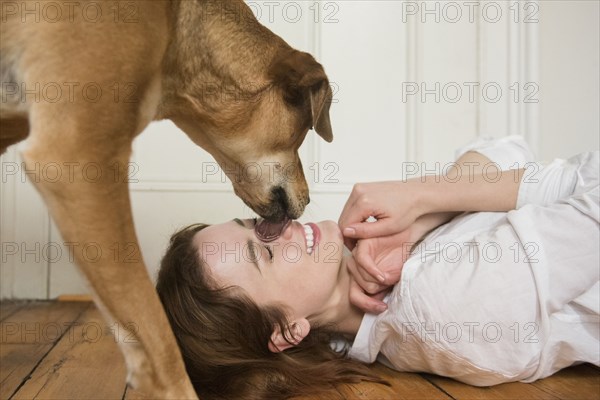 Dog licking nose of Caucasian woman laying on floor