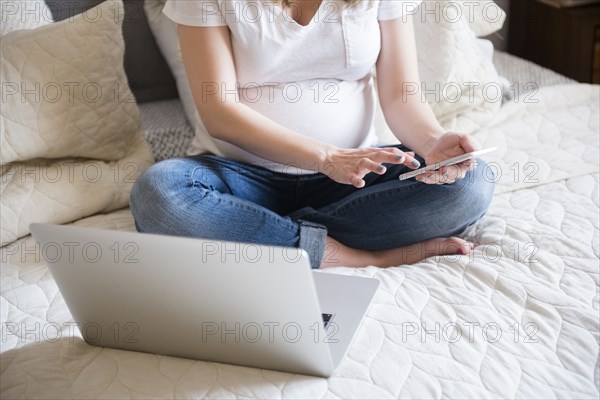 Caucasian expectant mother texting on cell phone on bed