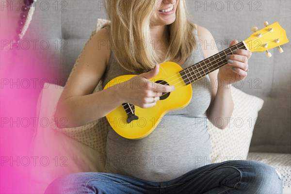 Caucasian and expectant mother playing small yellow guitar