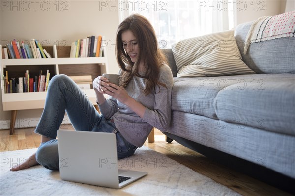 Caucasian woman sitting on floor with coffee and laptop