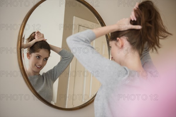 Reflection of Caucasian woman in mirror pulling back hair
