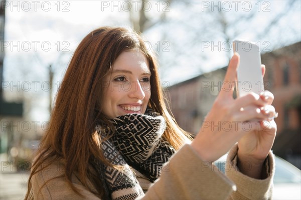 Caucasian woman wearing scarf posing for cell phone selfie