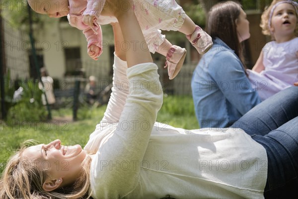 Caucasian mother laying in grass lifting baby daughter