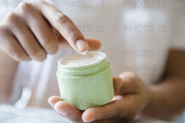 Close up of African American woman dipping finger in lotion jar