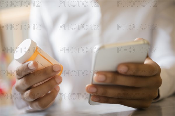 Hands of African American woman holding cell phone and pill bottle