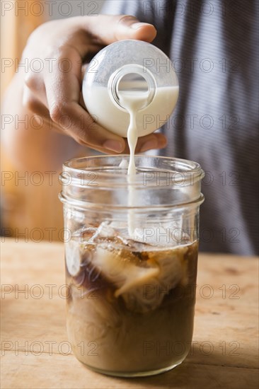 African American woman pouring milk into jar of coffee