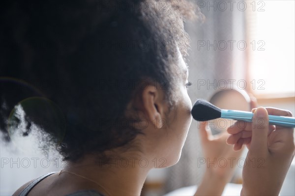 African American woman applying blush to cheek