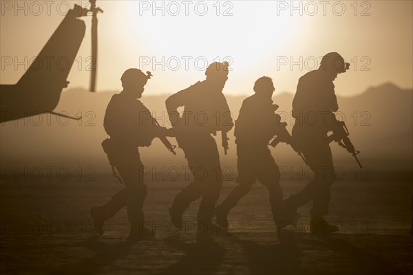Silhouette of soldiers near helicopter in desert landscape