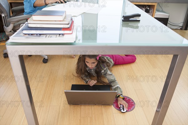 Mixed race girl sitting under desk in home office