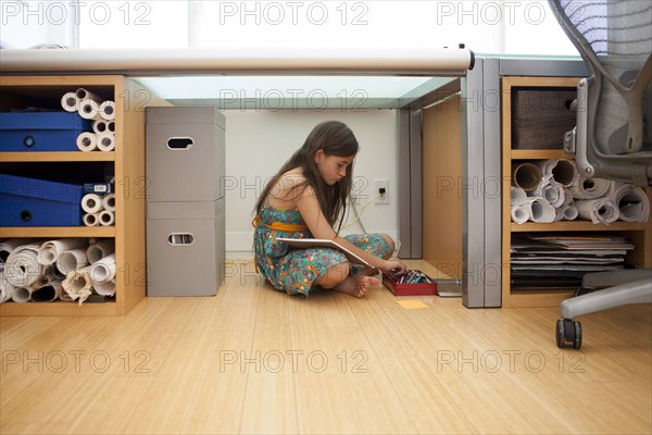 Mixed race girl sitting under desk in home office