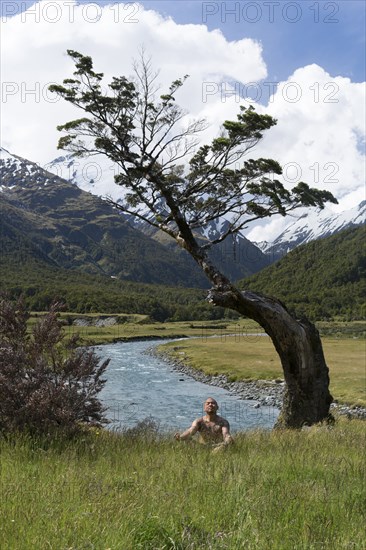 Chinese man meditating near mountain river