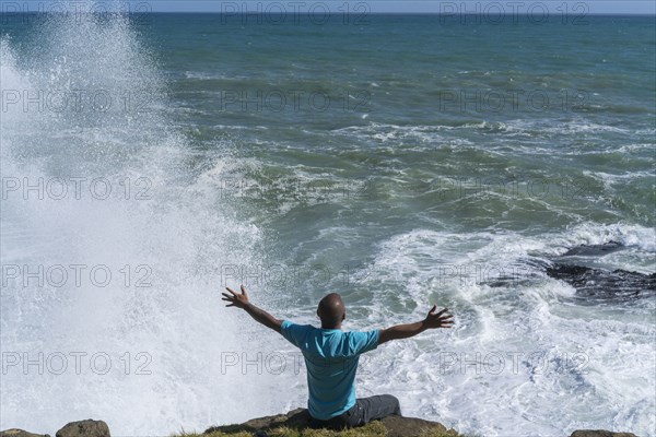 Chinese man sitting on cliff at ocean