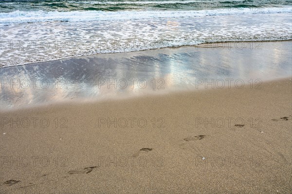 Footprints and sea wave on sandy beach