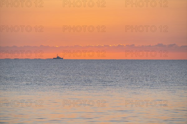 Calm sea at sunrise with fishing boat in distance