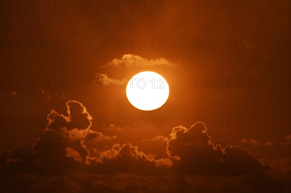 Bright sun at sunset with clouds against orange sky