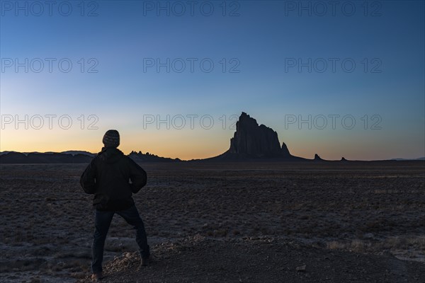 Silhouette of man looking at Ship Rock at sunset
