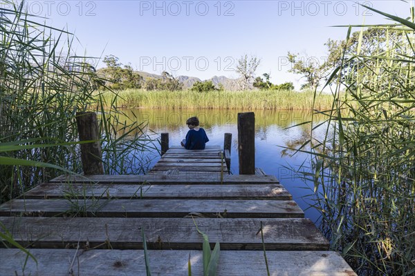 Boy sitting on wooden pier