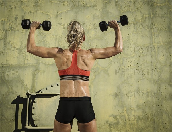 Rear view of athlete woman exercising with dumbbells