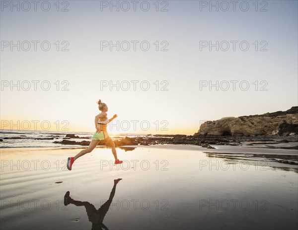 Rear view of athlete woman running on beach at sunset