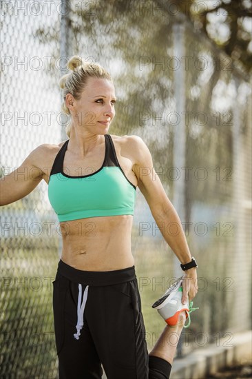 Athlete woman in sports clothing stretching at fence