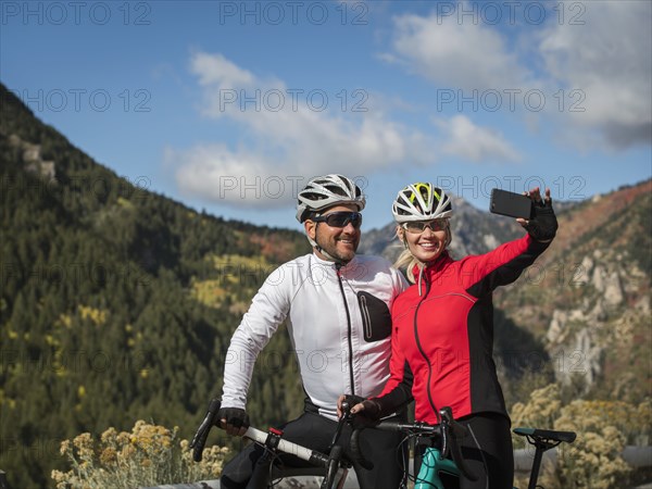 Smiling couple with bicycles taking selfie in mountain landscape