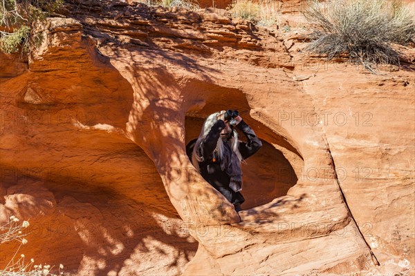 Senior hiker using binoculars in rock opening in sandstone cliff