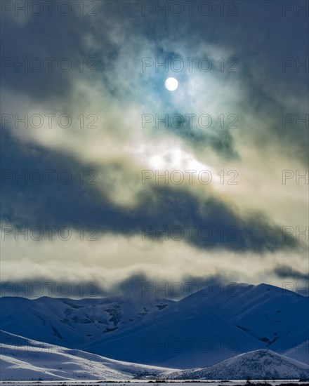 Sun shining through clouds above snowcapped mountains