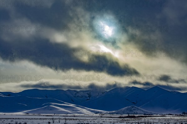 Sun shining through clouds above snowcapped mountains